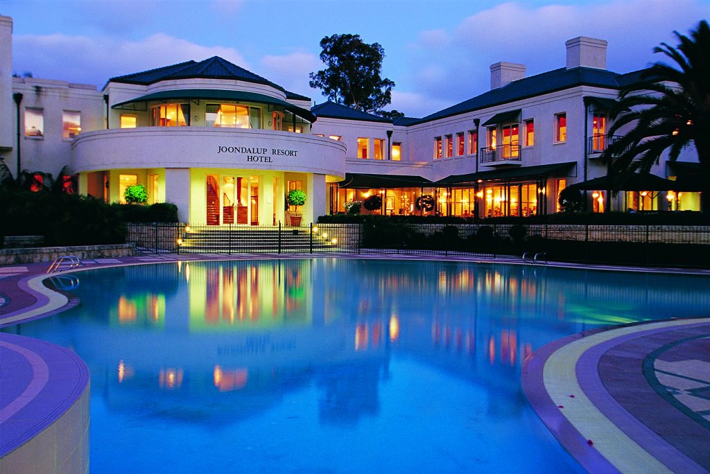 Joondalup Resort Hotel at dusk, with a large illuminated swimming pool reflecting the building's lights.