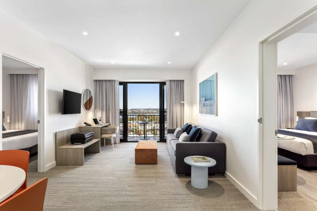 Modern hotel suite with a living area, two bedrooms, and a balcony with a city view.
