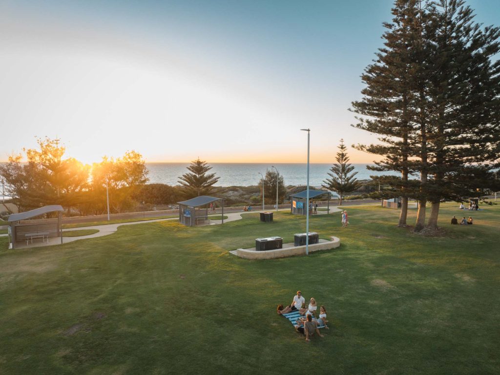 People relaxing in Tom Simpson Park Mullaloo at sunset, with the ocean in the background.